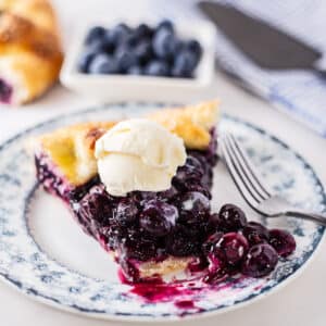 Tasty blueberry galette sliced and served on blue floral dessert plate with a small scoop of ice cream and a bite cut away.