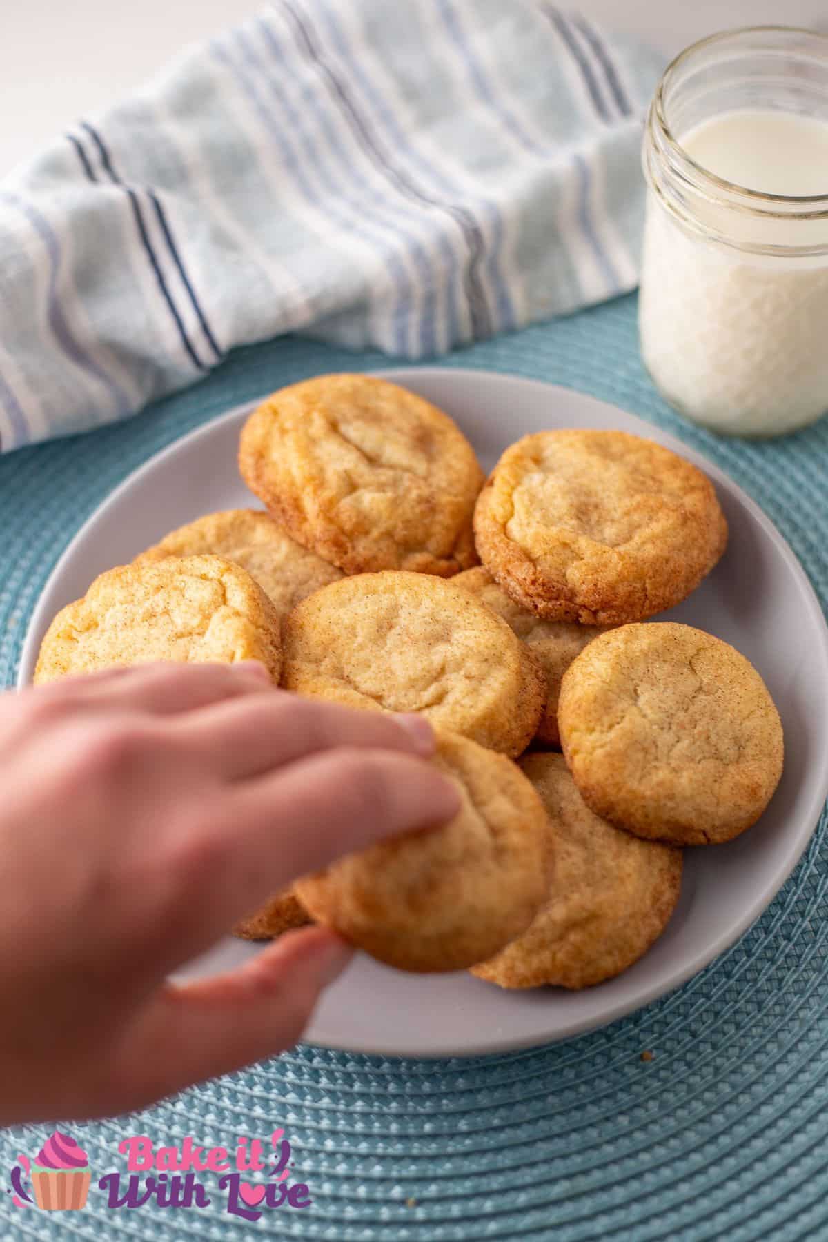 Plated snickerdoodles without cream of tartar served with a glass of milk and being picked up to eat.