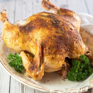 Square image of bage roasted chicken on a platter with parsley.