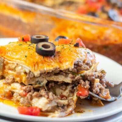 Square image of beef enchilada casserole sliced on a plate.
