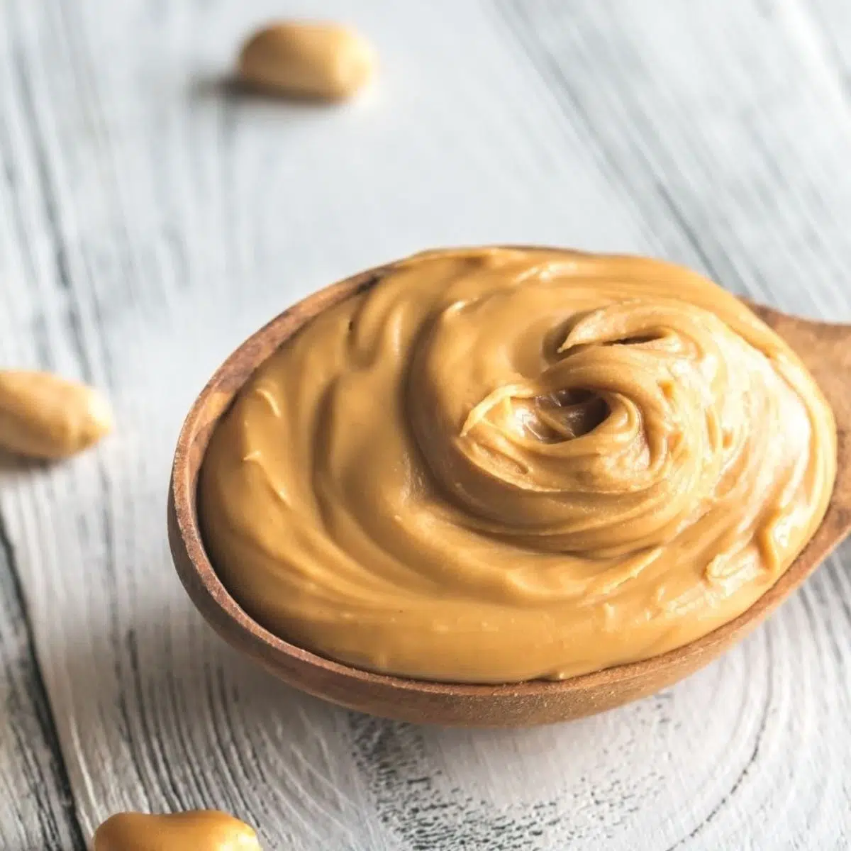 Beste Erdnussbutter-Ersatzideen und -alternativen mit einem Löffel voll Erdnussbutter auf grauem Holzhintergrund.