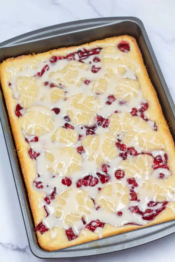 Process image 14 showing cherry pie bars in pan with glaze drizzled over.
