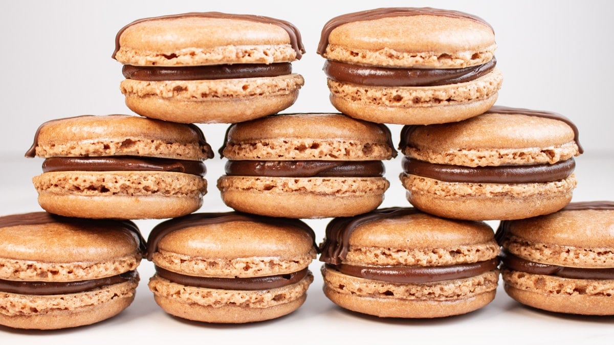 Tasty chocolate macarons stacked on a light background.