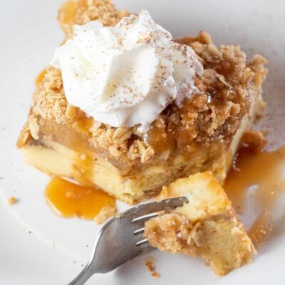 Tall image of a slice of apple pie french toast casserole with whipped cream on top.