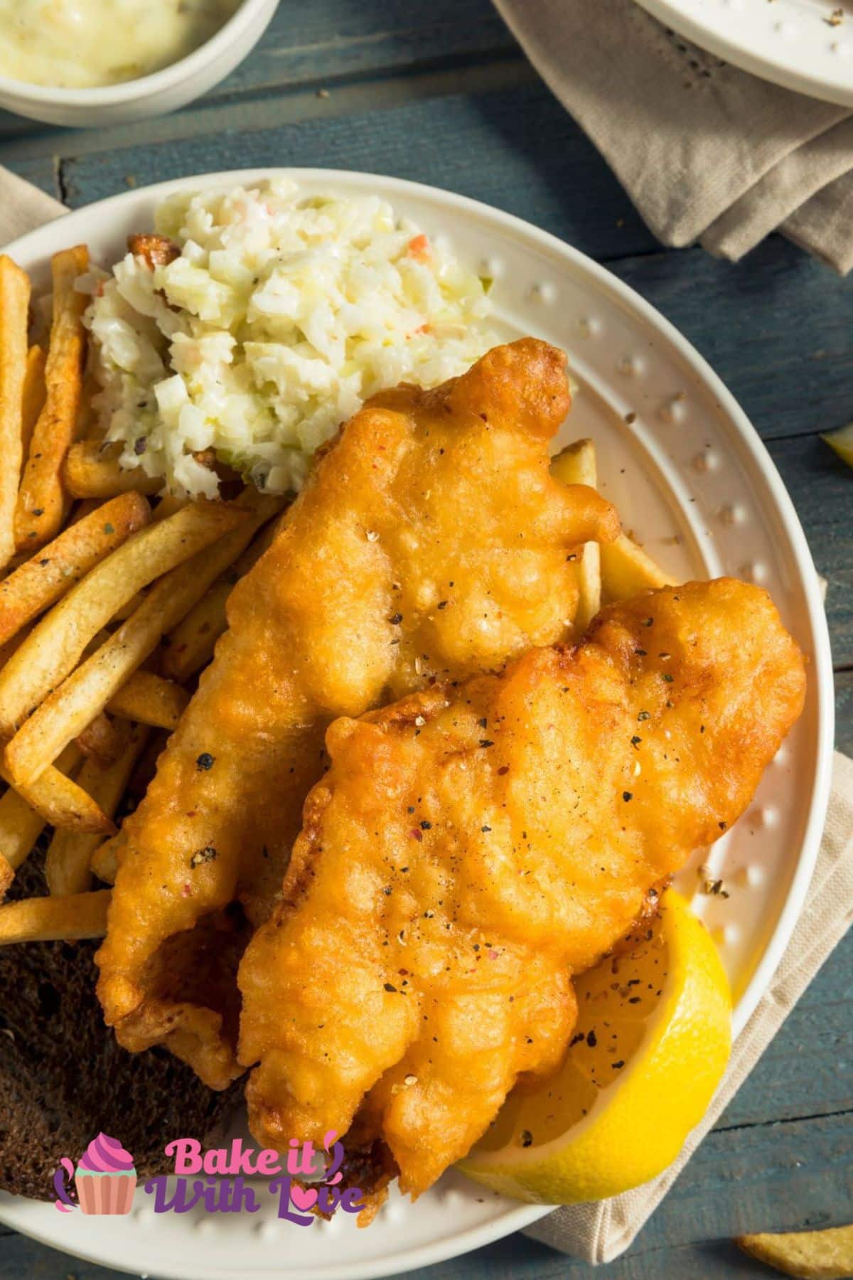 Tall image of deep fried catfish on a plate with coleslaw and fries.