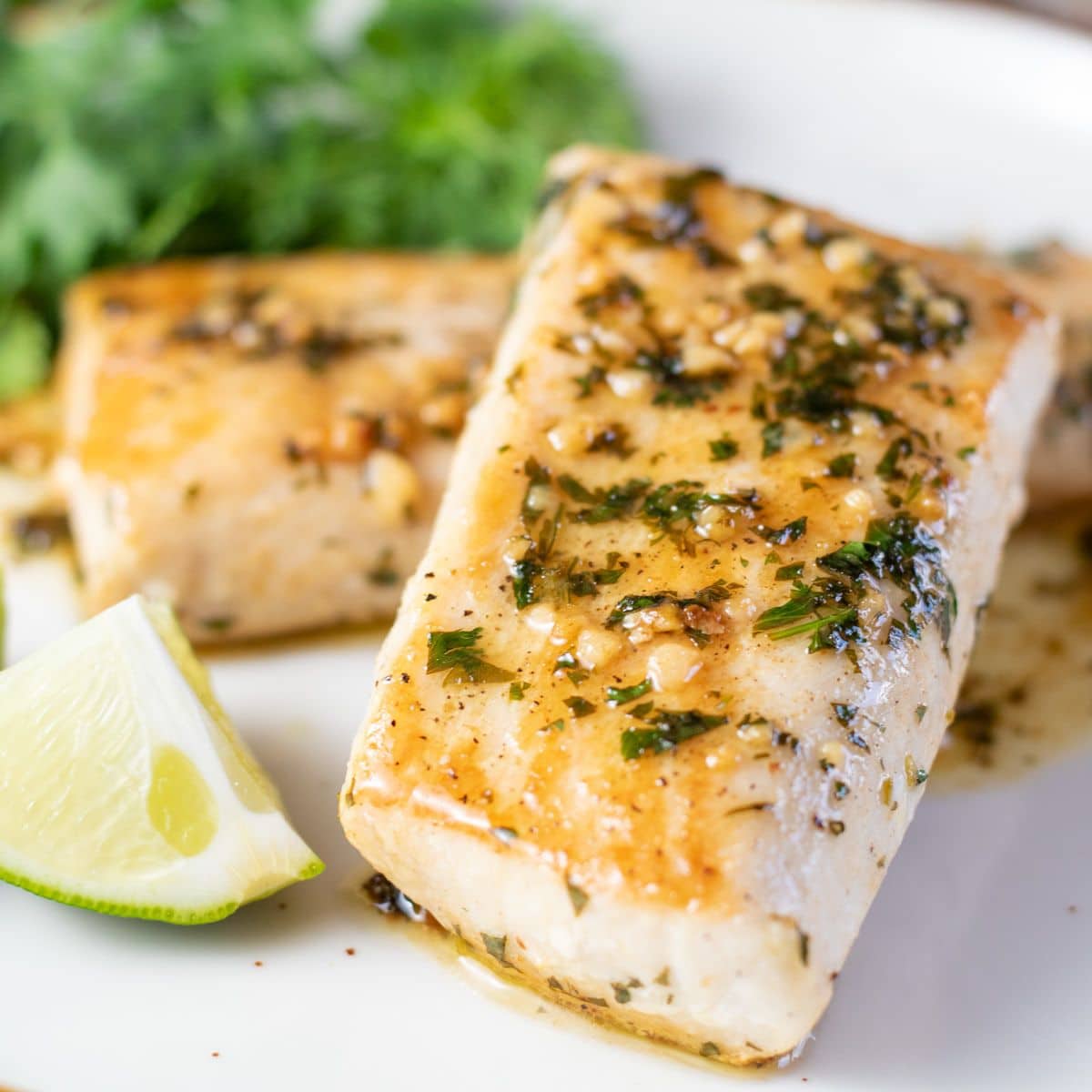 Square image of cooked fish on a white plate with lemon.