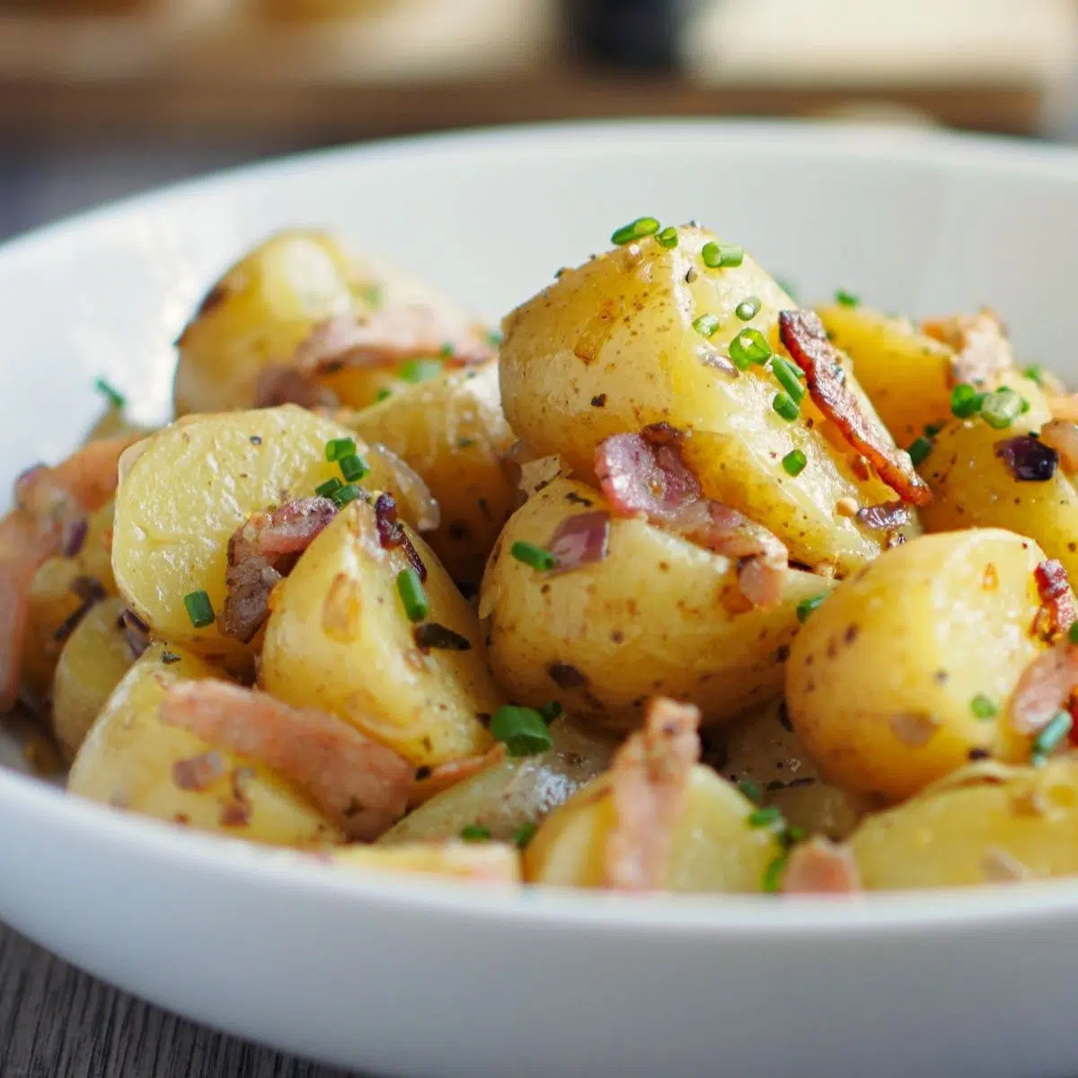 Квадратное изображение немецкого картофельного салата в белой миске.