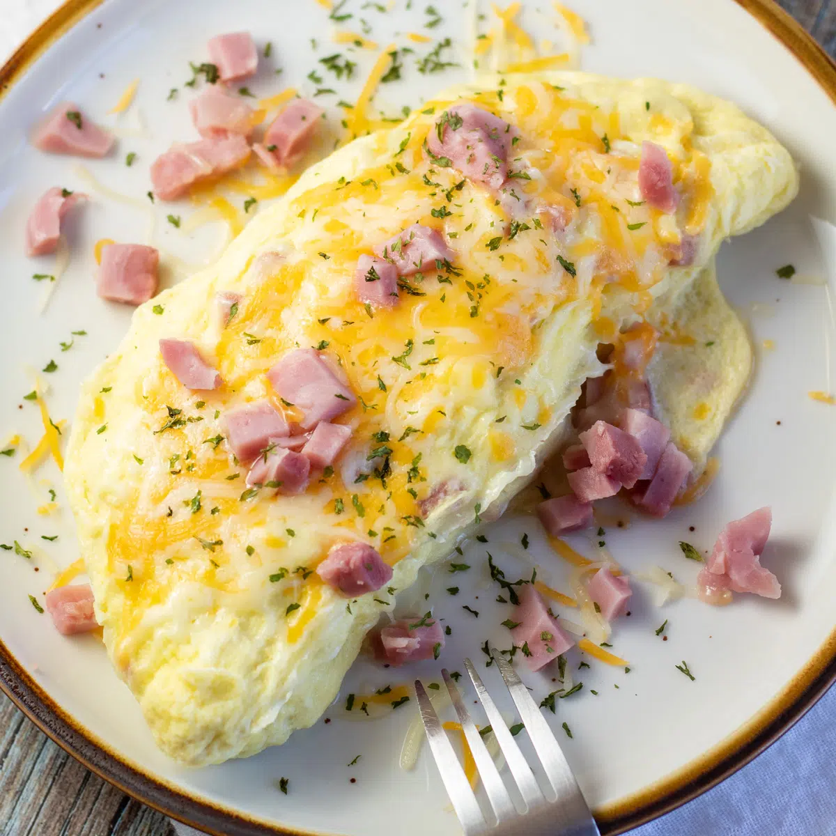Square image of an omelet on a plate with ham & cheese.