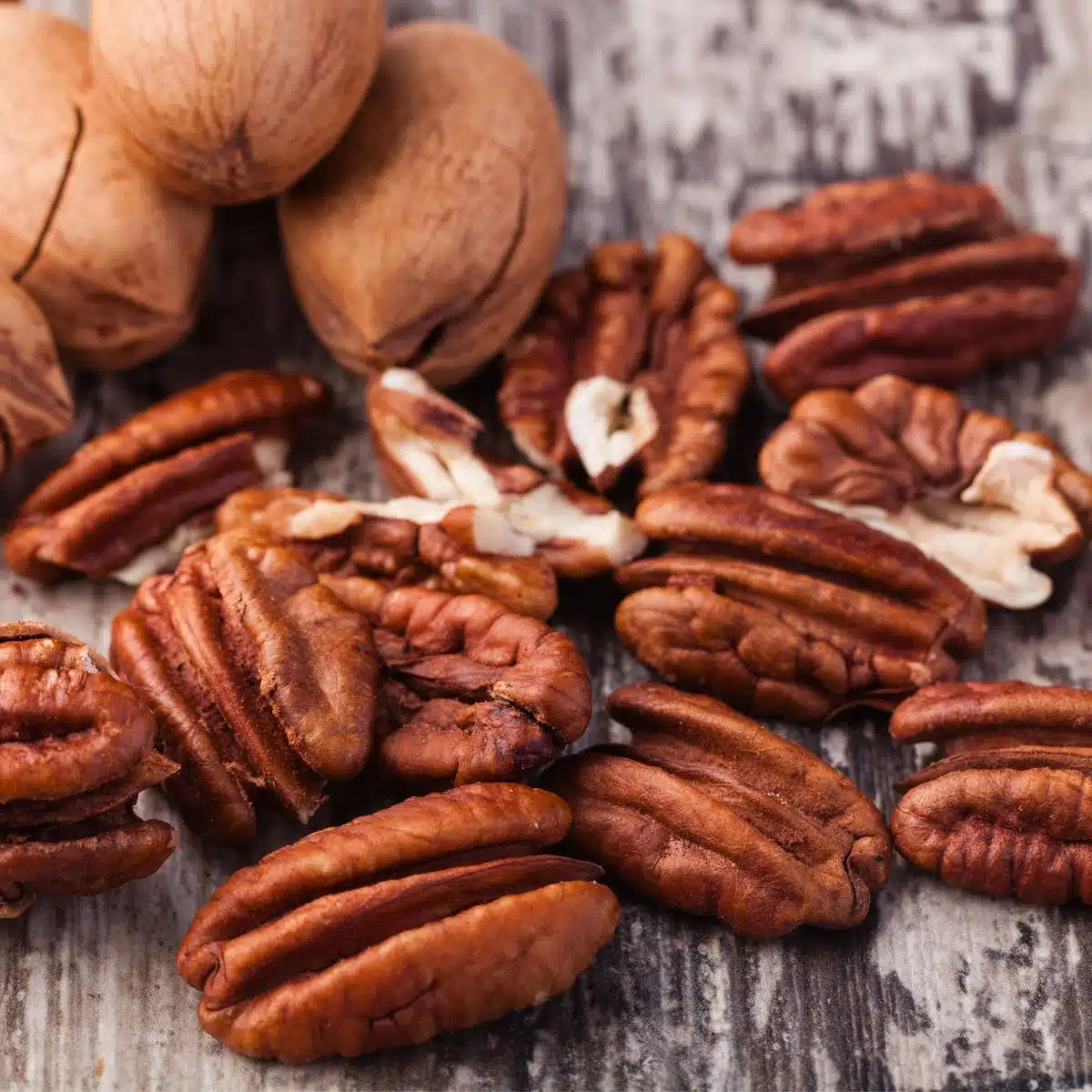 Square image of pecans on grey wood background.