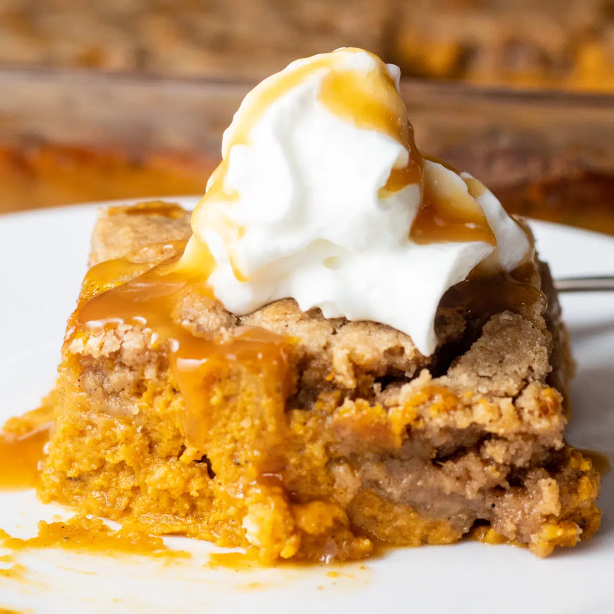 Square image of a slice of pumpkin dump cake on a white plate.