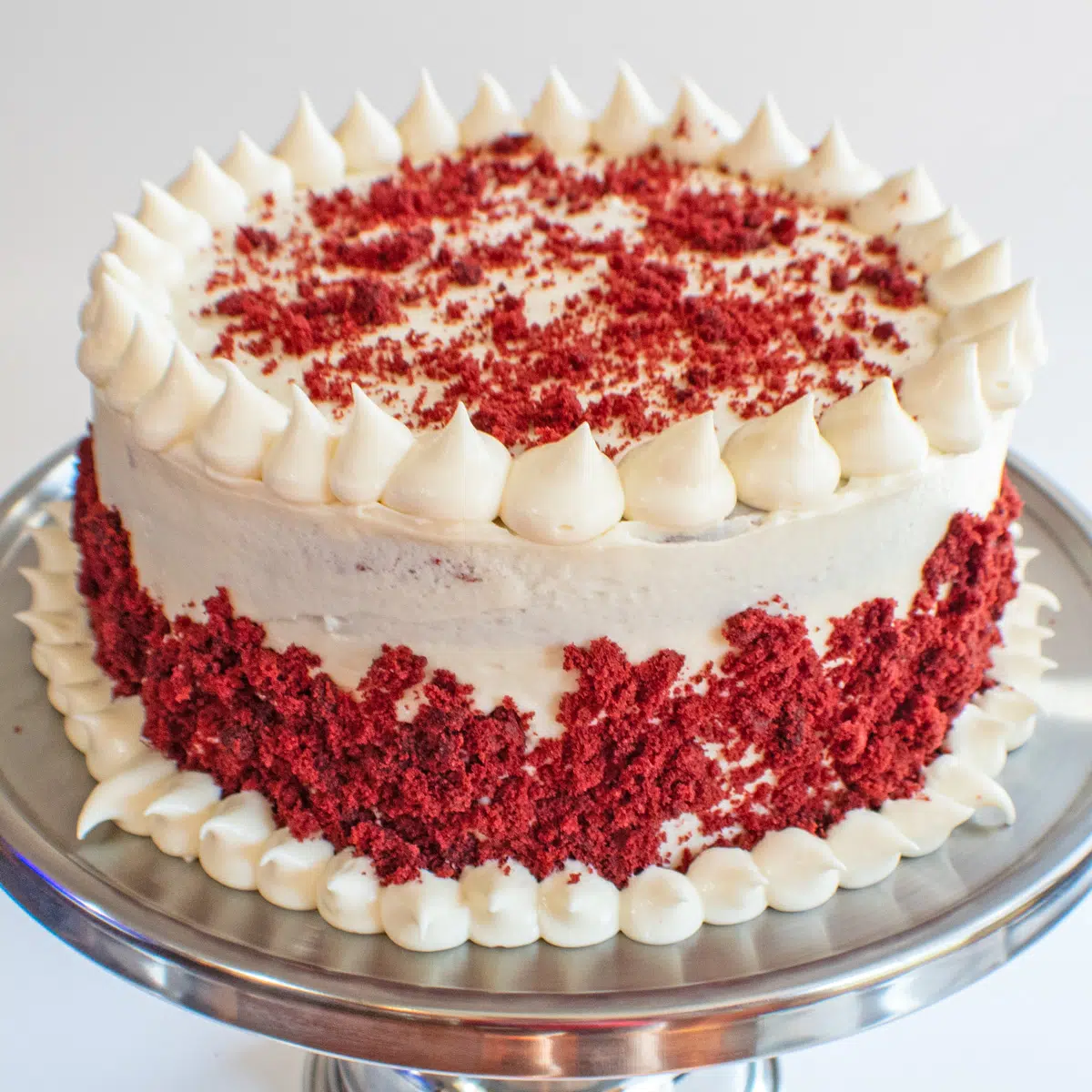 Imagem quadrada de bolo de veludo vermelho com cobertura de cream cheese.