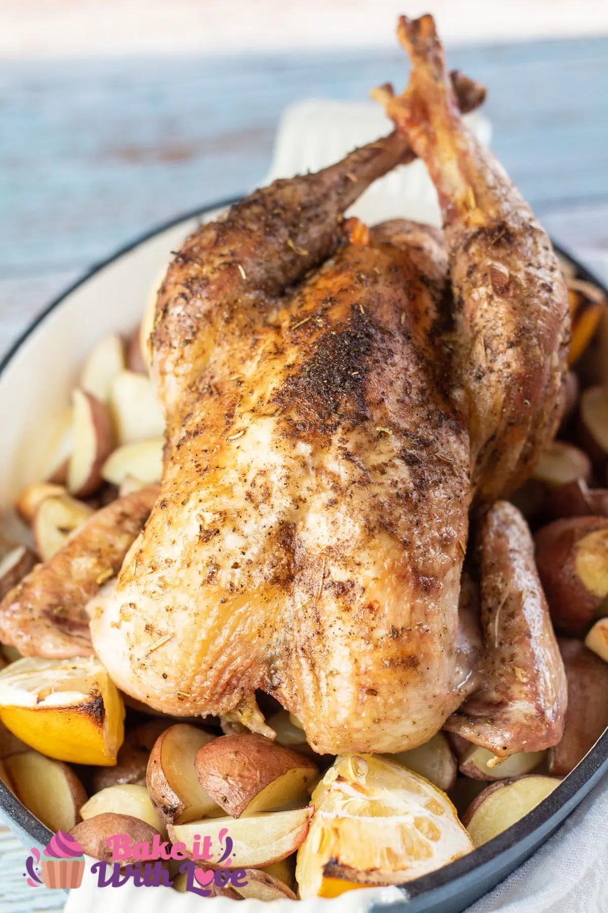 Tall image of roasted pheasant in roasting pan with potatoes and lemons.