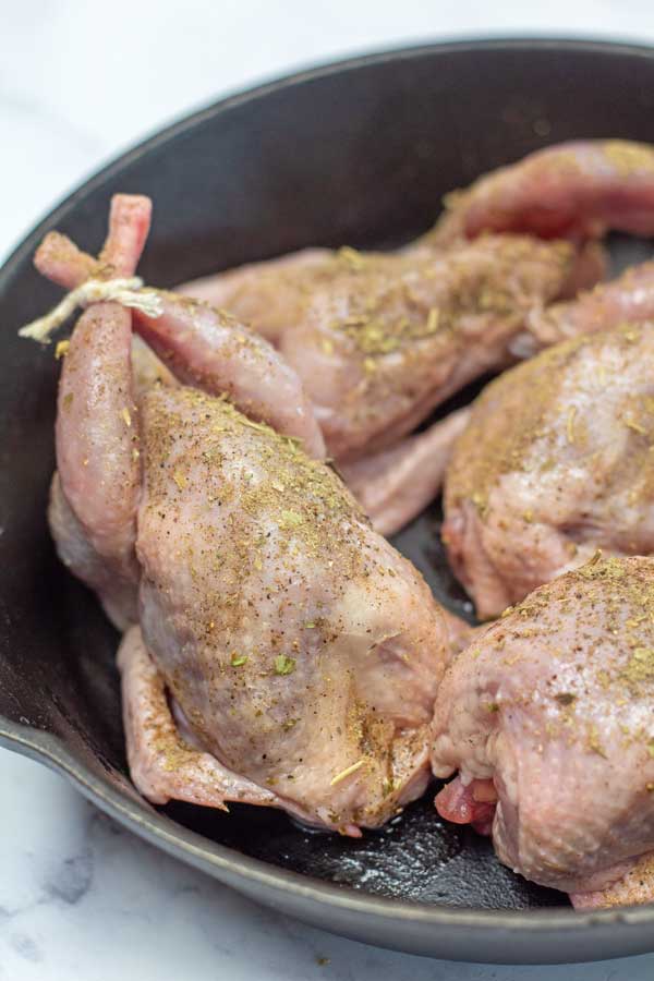 Process image 2 showing trussed and seasoned quail in a cast iron pan before roasting.