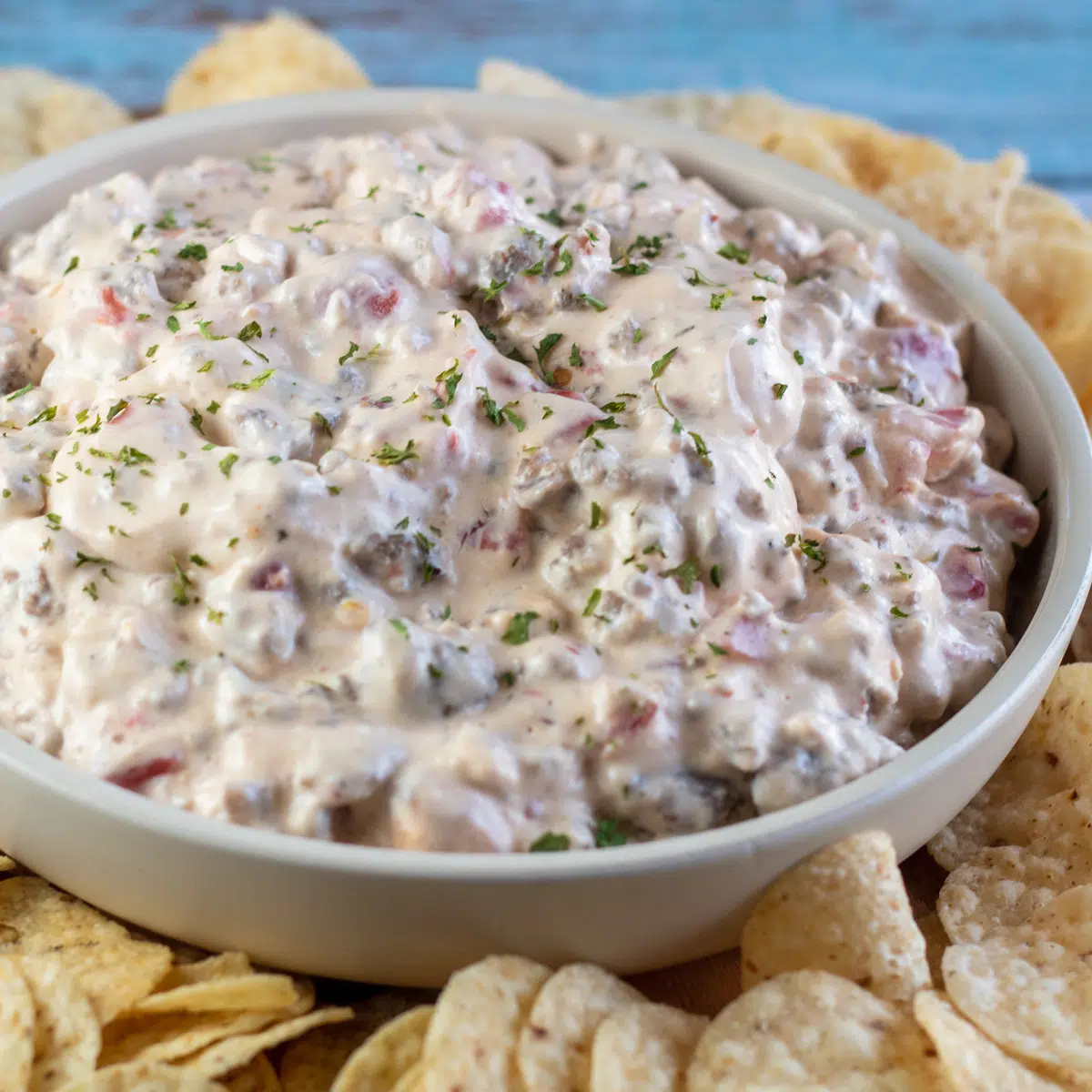 Square image of sausage cream cheese dip in a bowl with chips around bowl.