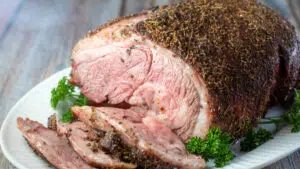 Wide image of a smoked boneless lamb leg on a white platter.