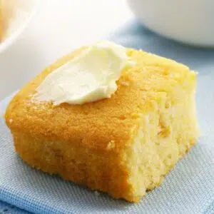 Square image of sour cream cornbread on a blue plate with a pat of butter.
