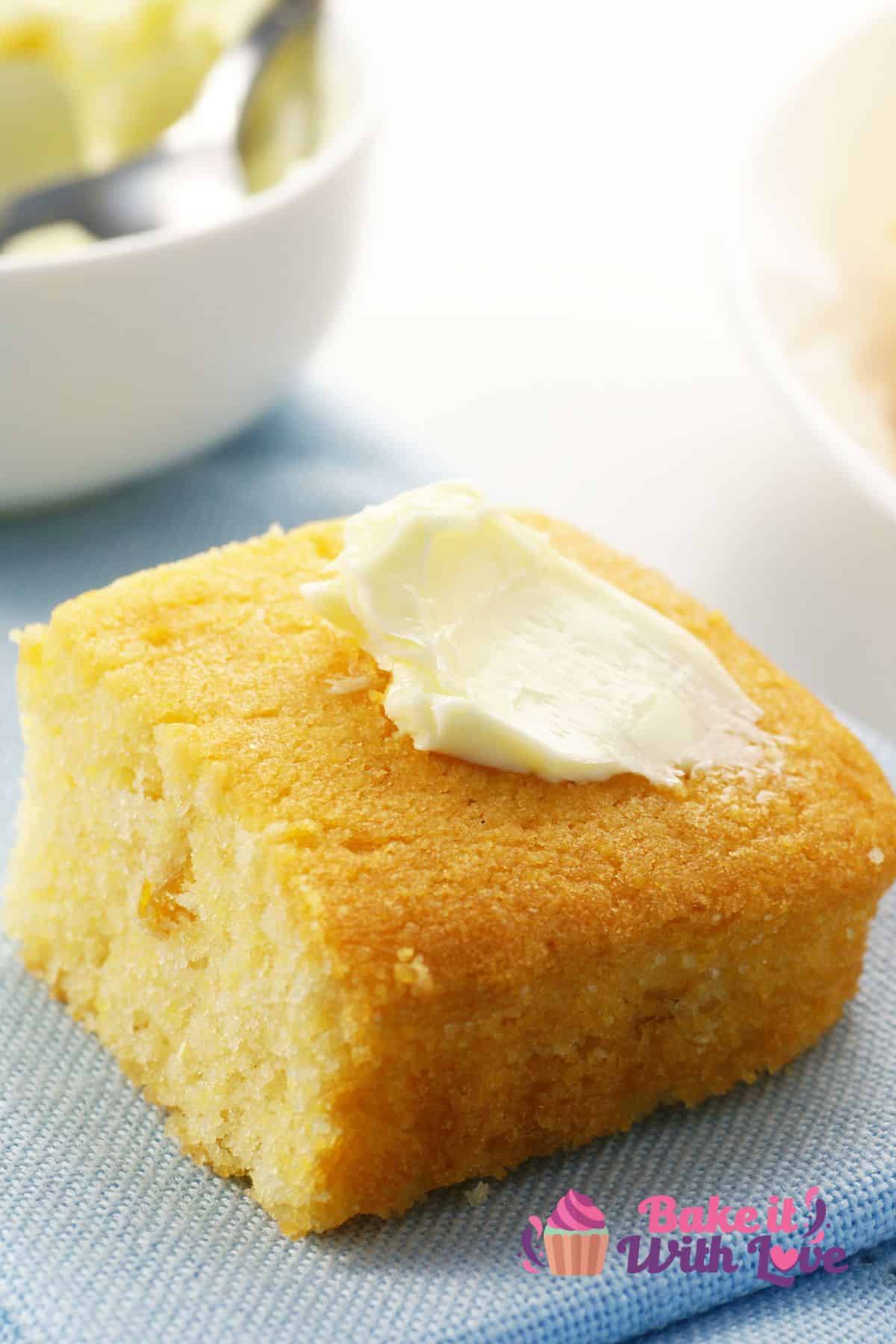 Tall image of sour cream cornbread on a blue plate with a pat of butter.