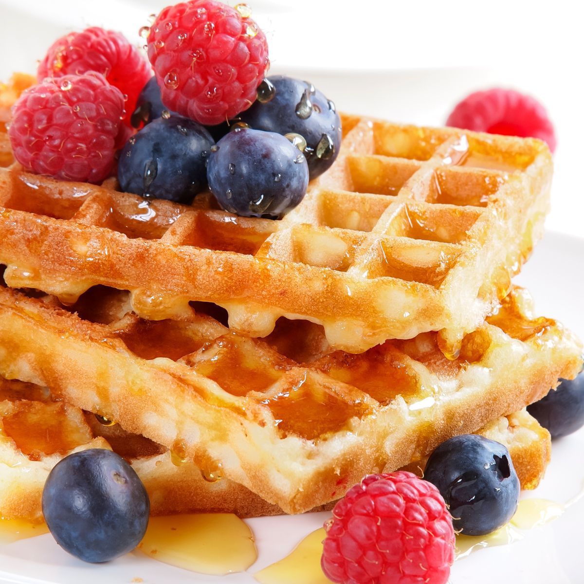 Square image showing waffles with fruit and syrup.
