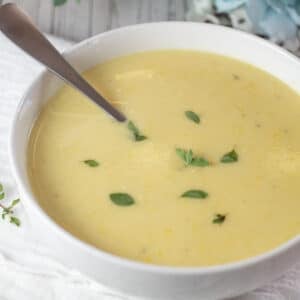 Square image of creamy yellow squash soup in a white bowl.