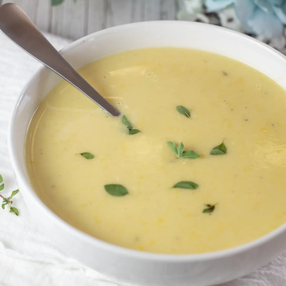 एक सफेद कटोरे में मलाईदार पीले स्क्वैश सूप की चौकोर छवि।