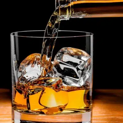Square image showing Irish whiskey being poured into a glass with ice.