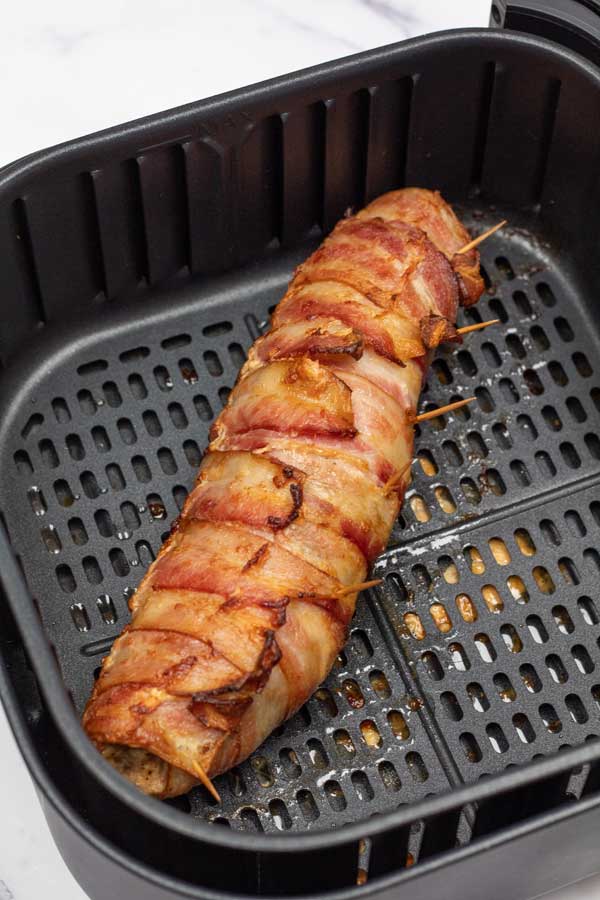 Process image 6 showing cooked bacon wrapped pork tenderloin in air fryer basket.