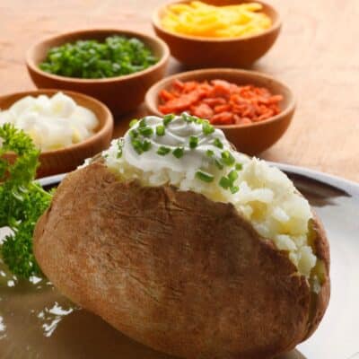 Vierkant beeld met gepofte aardappel met verschillende toppings op de achtergrond.