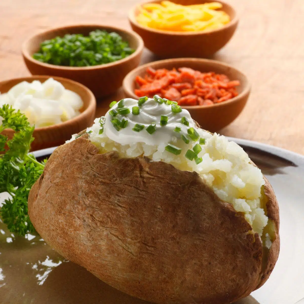 Imagen cuadrada que muestra patatas al horno con diferentes ingredientes en el fondo.