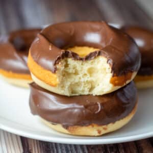 Square image of chocolate fosted baked donuts on a white plate.