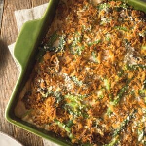 Square image of green bean casserole on a green baking dish.