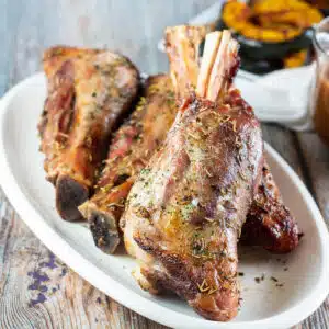 Square image of a white serving platter with grilled lamb shanks.