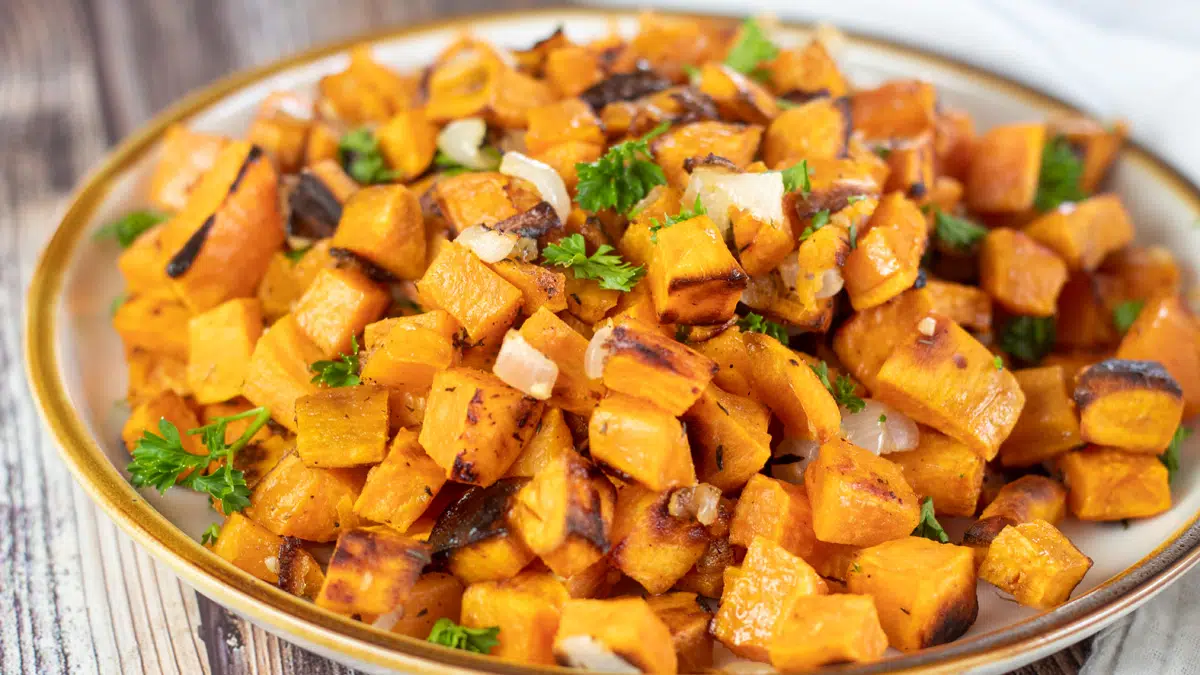 Wide image showing roasted sweet potatoes and onions in a bowl.
