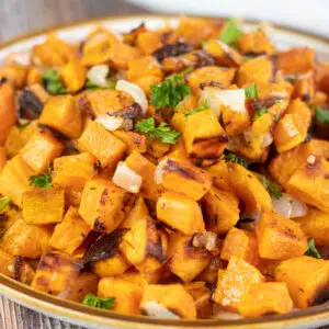 Square image showing roasted sweet potatoes and onions in a bowl.