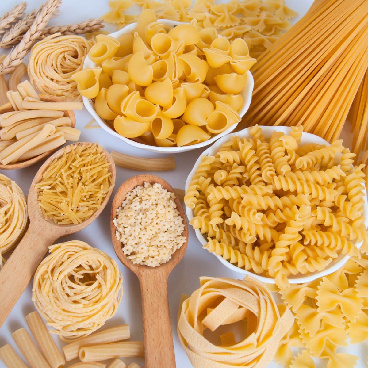 Kvadratna slika raznih vrsta tjestenine na bijeloj pozadini.