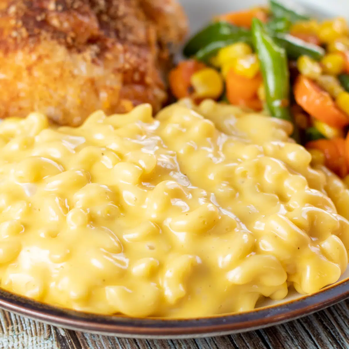 Firkantet billede, der viser velveeta mac & cheese på en tallerken med kylling og grøntsager.