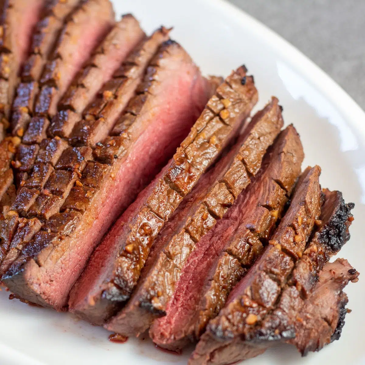 Square image of sliced london broil on a white serving platter.