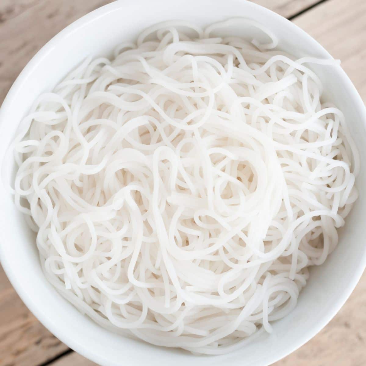 Square image of a white bowl full of vermicelli.
