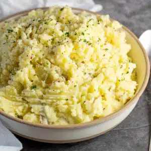 Square image showing a large bowl of yellow mashed potatoes.