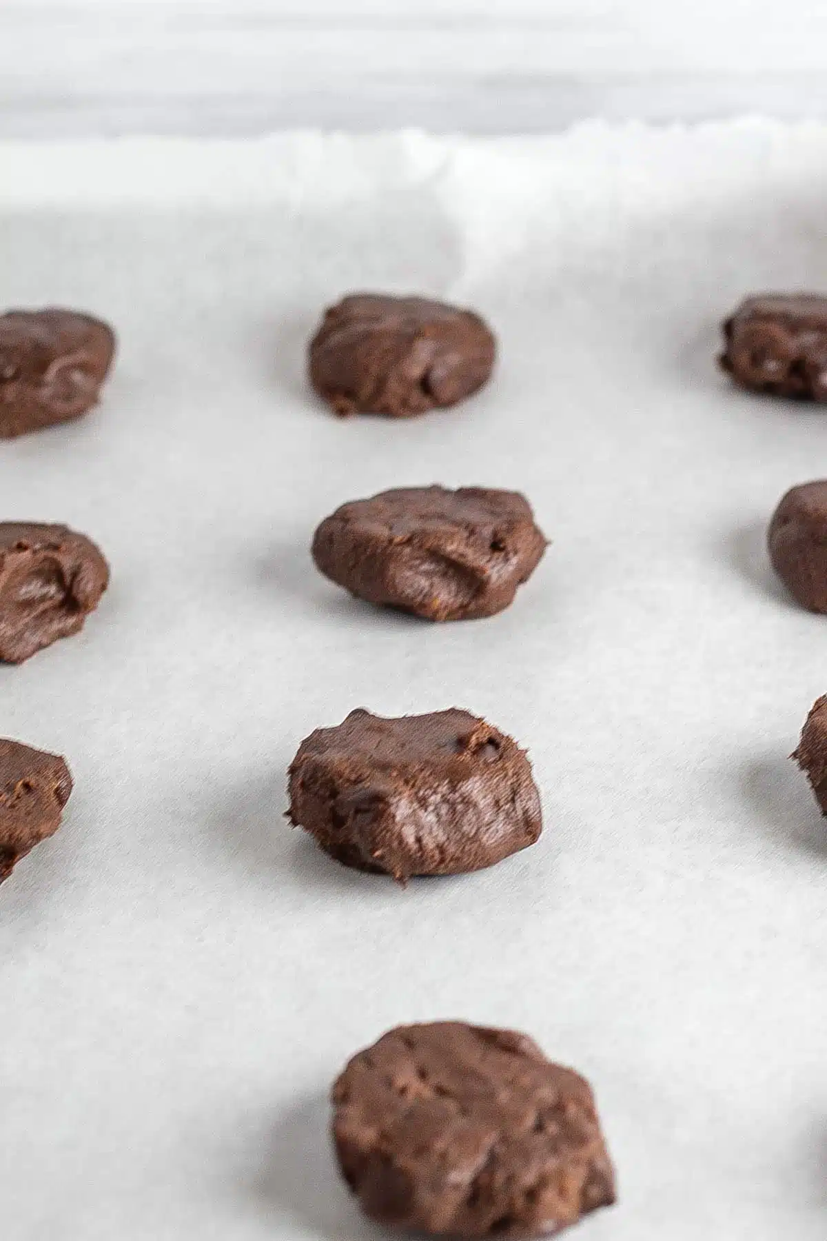 Chocolate peppermint cookies process photo 9 shaped chocolate cookie dough on parchment paper lined baking sheet.
