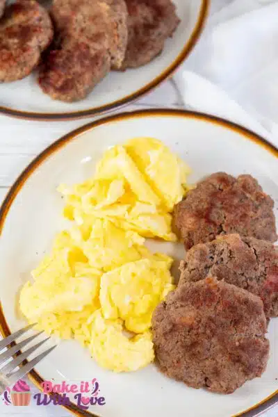 Tall image showing breakfast sausage patties on a plate with scrambled eggs.