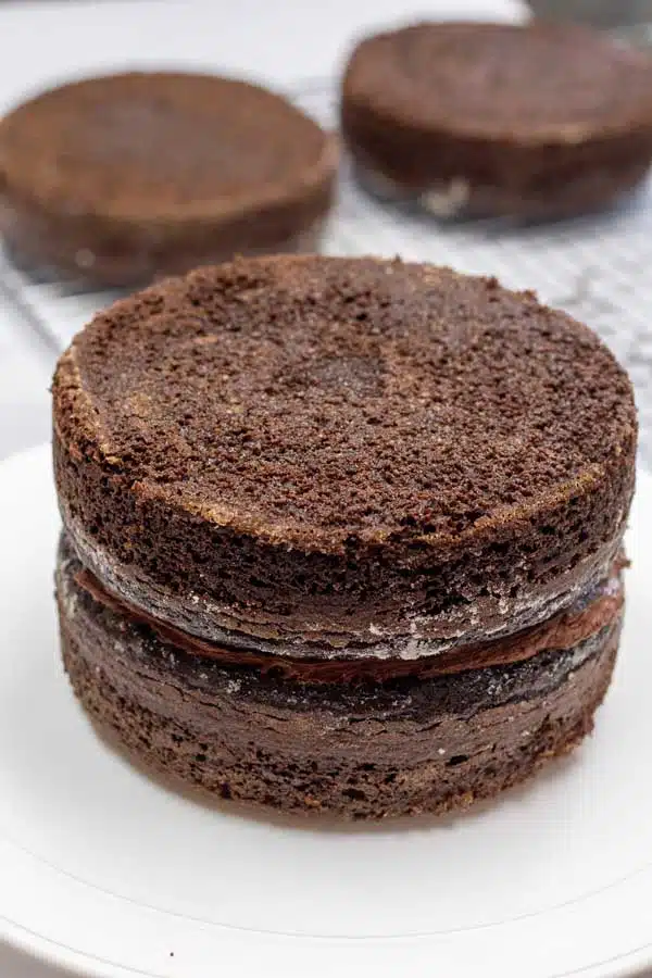Process image 15 showing chocolate cake rounds stacked with buttercream in between layers.