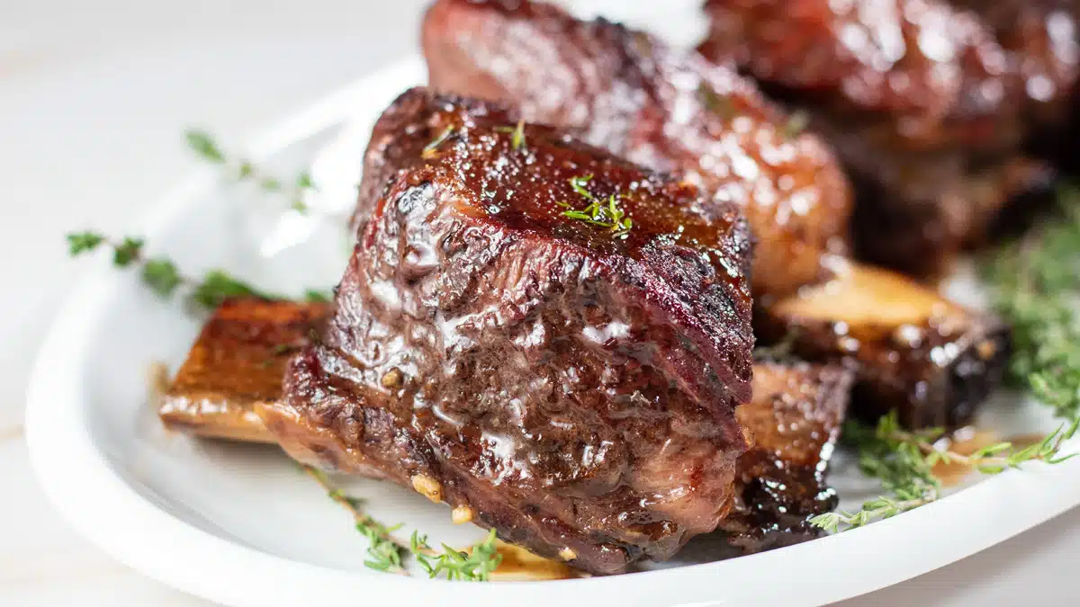 Wide image of crockpot beef short ribs on a white serving plate.