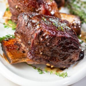 Close up square image of crockpot beef short ribs on a white serving plate.