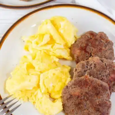 Tall image showing breakfast sausage patties on a plate with scrambled eggs.