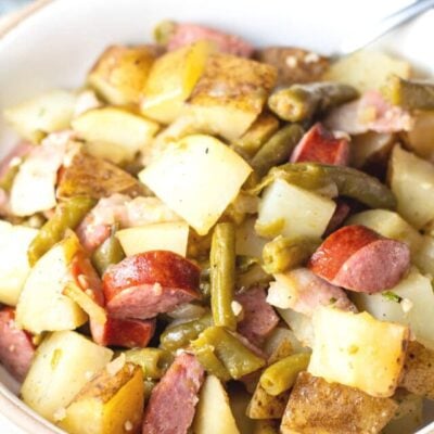 Tall image of green bean potato and sausage casserole in white bowl.