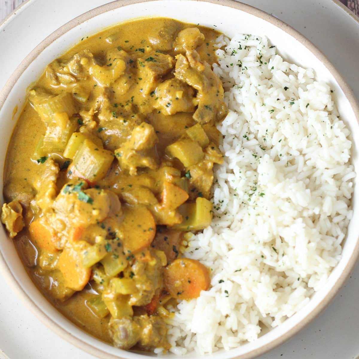 Kvadratna slika prikazuje bijelu zdjelu s kozjim curryjem i rižom.