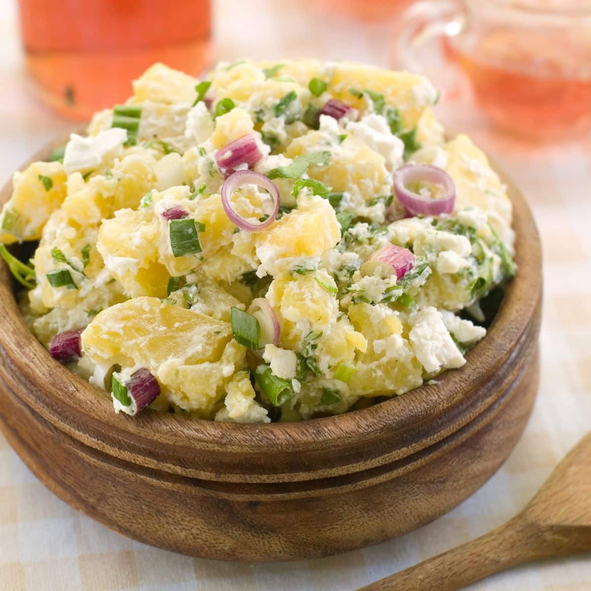 Meilleure recette de salade de pommes de terre classique à préparer pour toutes les occasions, servie dans un bol en bois sur fond clair.