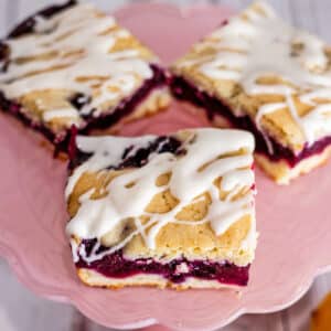 Best blueberry pie bars recipe with tasty iced pie bars on pink cake stand.