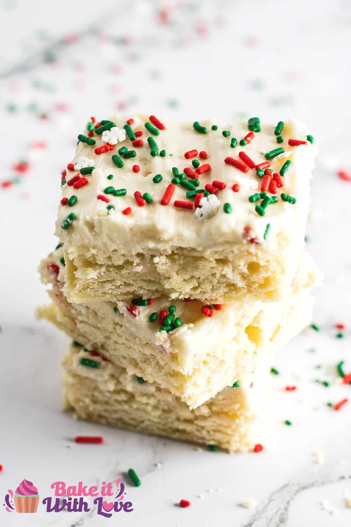 Best Christmas sugar cookie bars stacked on light marbled background with festive holiday sprinkles scattered around the trio of cookie bars.