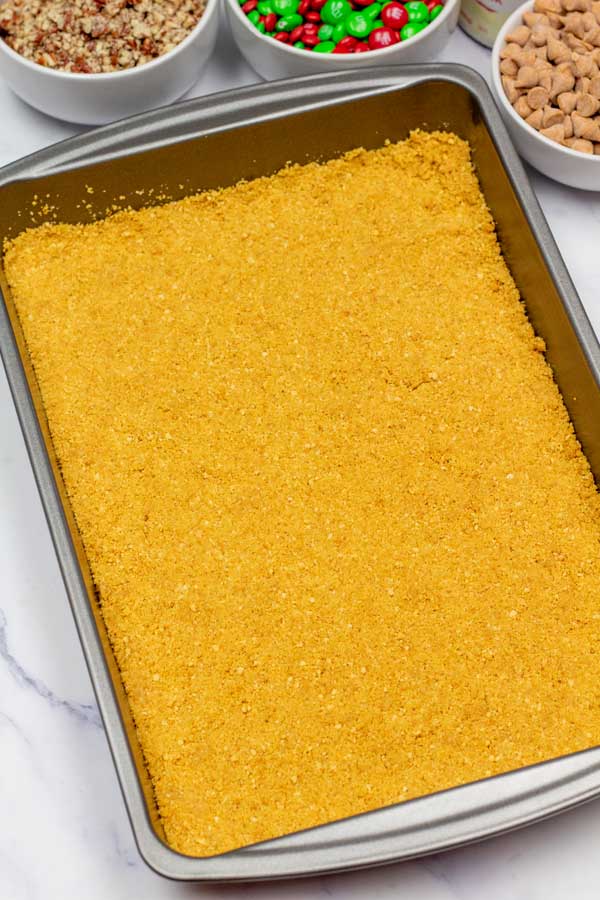Process image 4 showing graham cracker base pressed down into 9x13 baking dish.